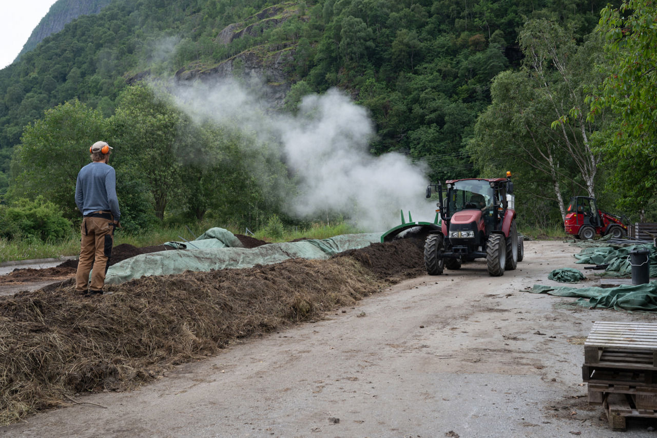 Elev ved Sogn Jord- og Hagebruksskule arbeider med kompostering og jordhelse, medan ein lærar følgjer arbeidet og traktor vender kompostranker i det grøne fjordlandskapet.
