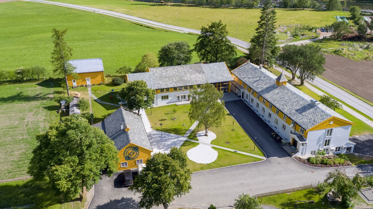 Skulegarden ved Sogn Jord- og Hagebruksskule i Aurland med undervisningsbygg, grøne jordbruksareal og økologisk gardstun sett ovanfrå.