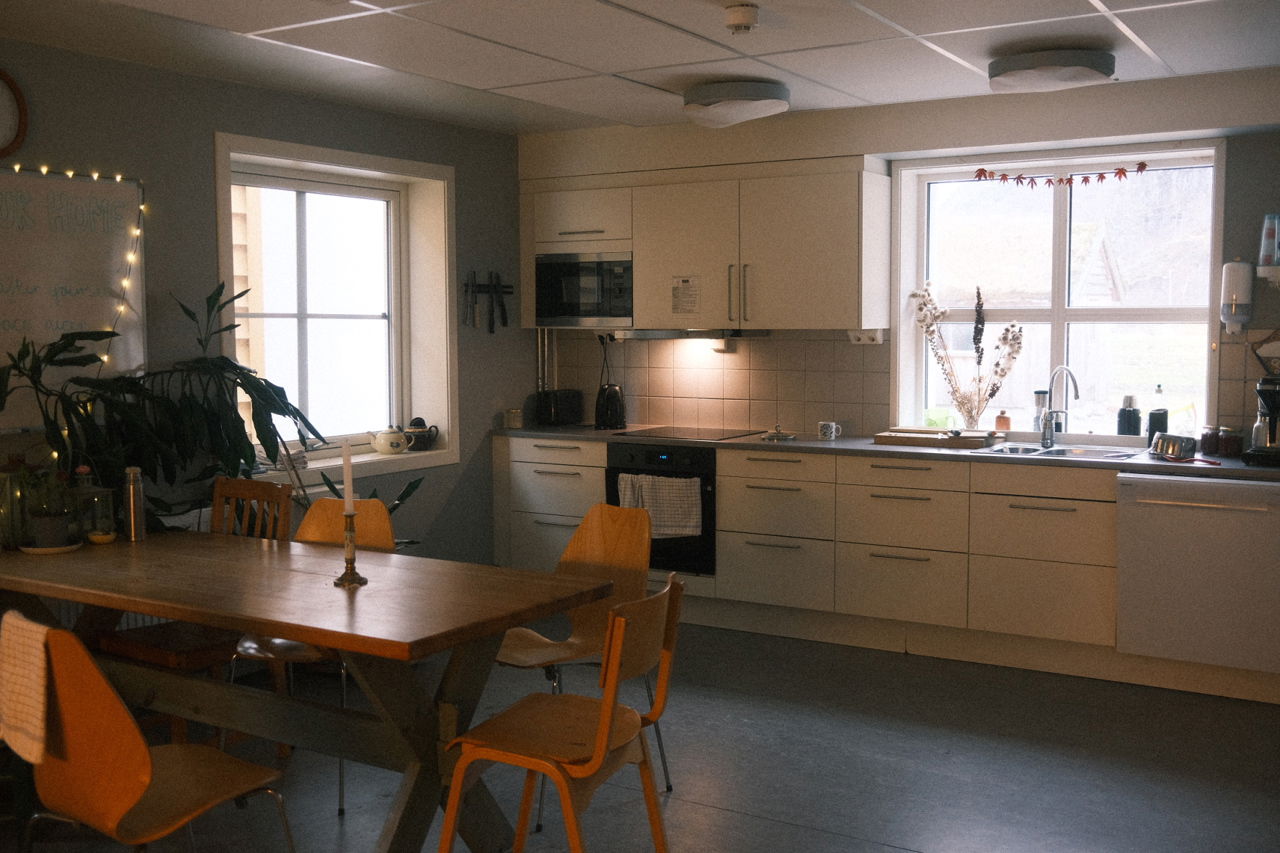 Felles kjøken på internatet med spisebord, kjøkenbenk og store vindauge.