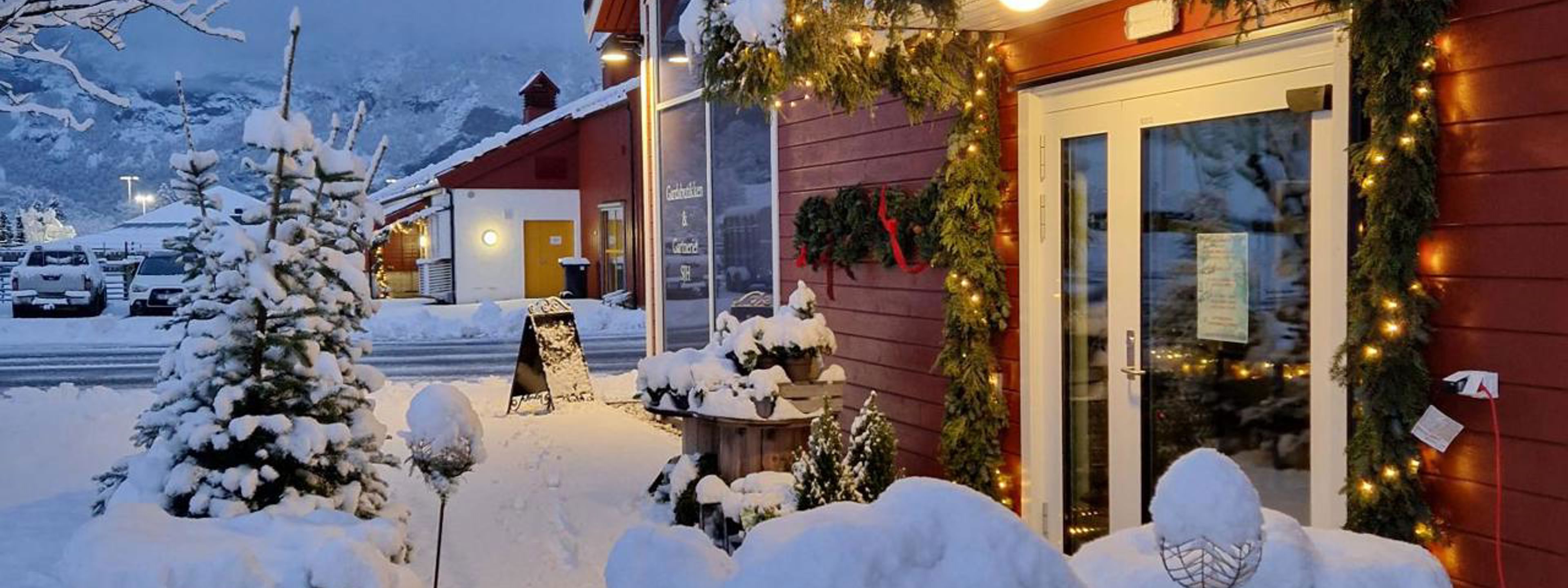 Åpen gårdsbutikk i førjulsstemning, med snø, granbar og varme lys ved inngangen.