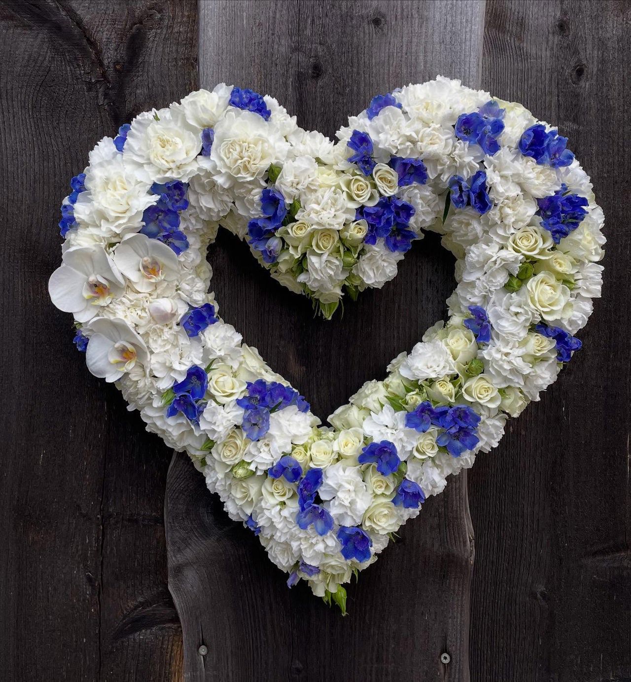 Heart-shaped funeral arrangement made of white roses, carnations and blue flowers by the floral department at SJH.