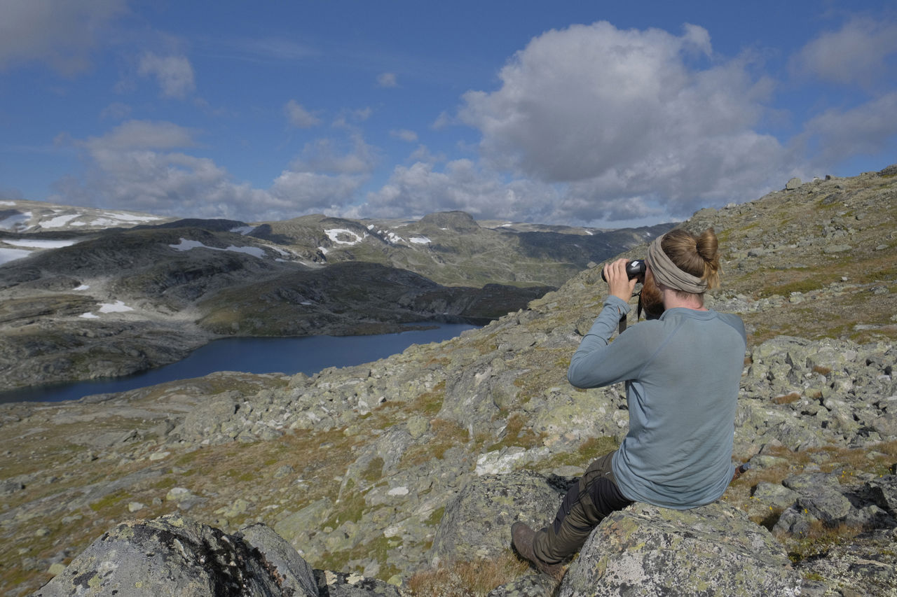 Elev sit på ein stein og ser utover høgfjellslandskap med kikkert – naturen som leikeplass for utforsking, observasjon og læring.