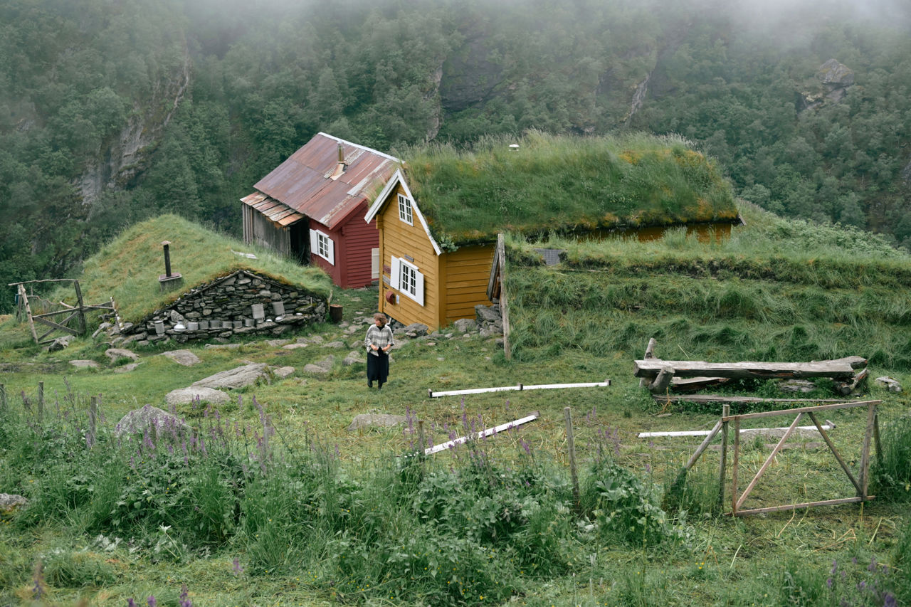 Tradisjonell stølsdrift med torvtak omgitt av fjell og grønt kulturlandskap.