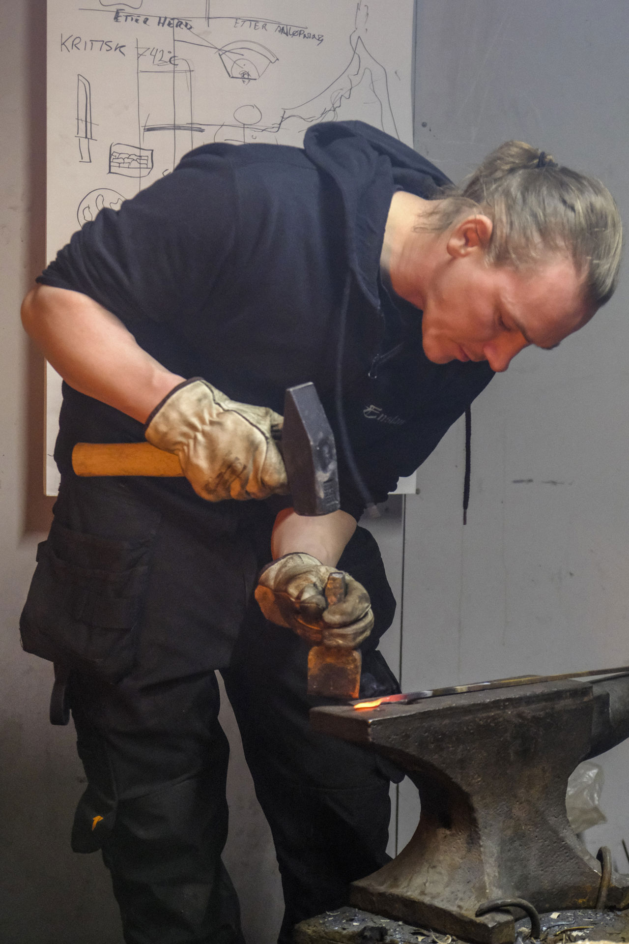 Elev arbeider med varmt metall i smia, medan ho formar emnet på ei ambolt.