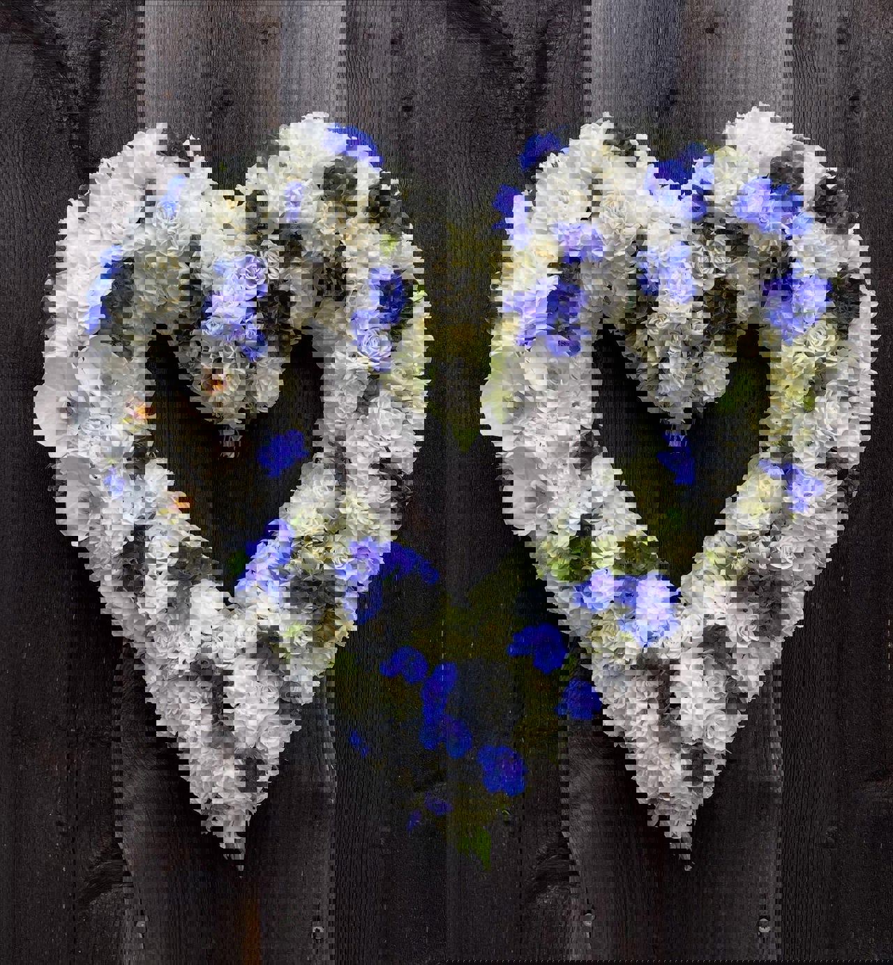Herzförmiger Trauerkranz aus weißen und blauen Blumen für einen würdevollen Anlass.
